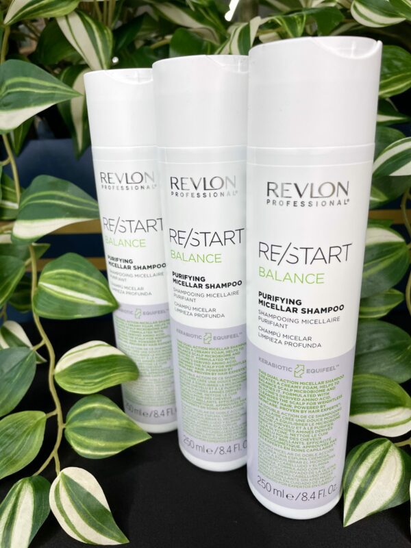 Three bottles of Re/Start Balance Purifying Micellar Shampoo are standing upright on a black surface, with green leafy plants in the background. Three bottles of Re/Start Balance Purifying Micellar Shampoo are standing upright on a black surface, with green leafy plants in the background.