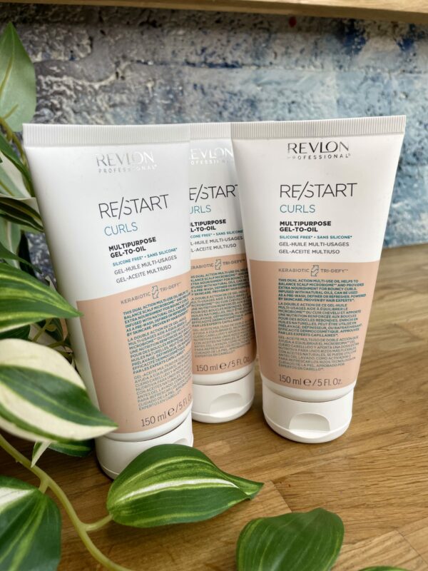Three tubes of Re/Start Curls Multipurpose Gel-to-Oil (150 ml each) stand upright on a wooden surface beside green houseplants, ideal for defining and nourishing curls. Three tubes of Re/Start Curls Multipurpose Gel-to-Oil (150 ml each) stand upright on a wooden surface beside green houseplants, ideal for defining and nourishing curls.