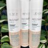 Three bottles of Re/Start Curls Nourishing Cleanser, 250 ml each, are displayed upright in front of lush green leafy plants.