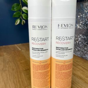 Two bottles of Re/Start Recovery Restorative Micellar Shampoo (250 ml each) sit side by side on a wooden surface, ideal for anyone seeking restorative hair care.