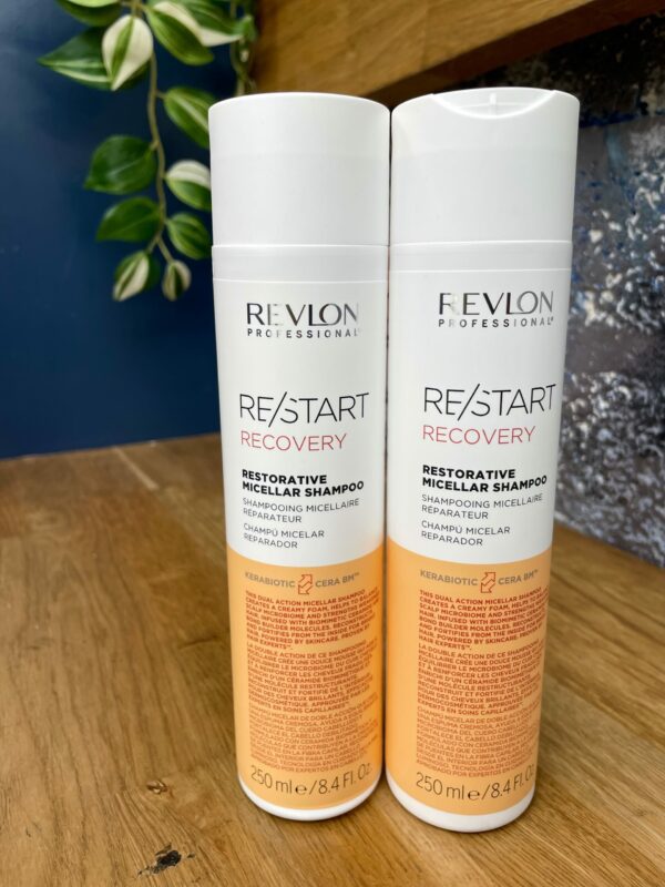 Two bottles of Re/Start Recovery Restorative Micellar Shampoo (250 ml each) sit side by side on a wooden surface, ideal for anyone seeking restorative hair care.