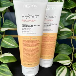 Two tubes of Re/Start Recovery Restorative Melting Conditioner, 200ml each, are displayed with green plants in the background, emphasizing their restorative care for damaged hair.