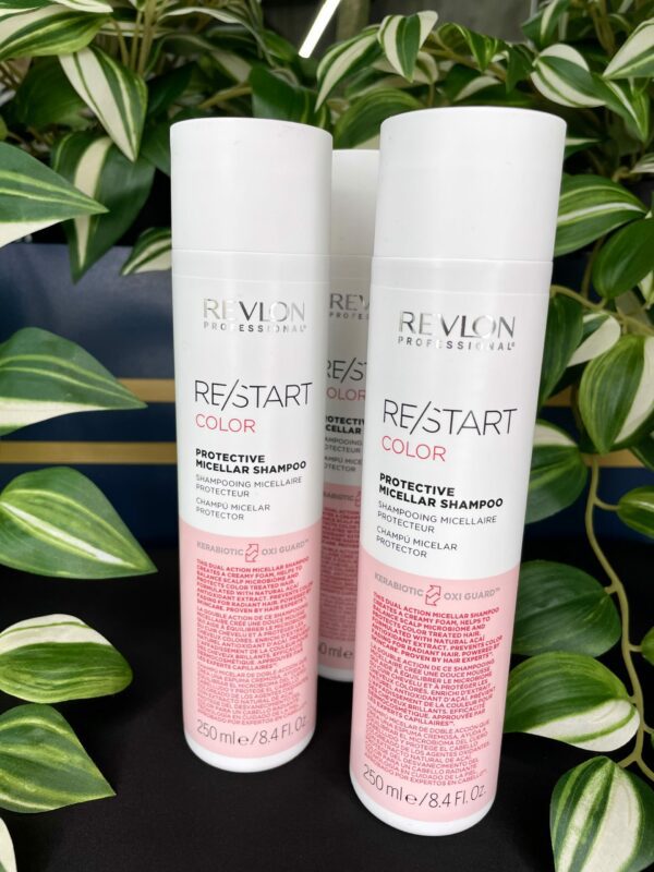 Three bottles of Re/Start Color Protective Micellar Shampoo are shown on a black surface with green and white leafy plants in the background, emphasizing the gentle care provided by this shampoo. Three bottles of Re/Start Color Protective Micellar Shampoo are shown on a black surface with green and white leafy plants in the background, emphasizing the gentle care provided by this shampoo.