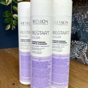 Three bottles of Re/Start Strengthening Purple Cleanser (250ml each) are displayed upright on a wooden surface, with a plant in the background.