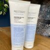 Two 200ml tubes of Re/Start Hydration Moisture Melting Conditioner are displayed on a wooden surface with a plant and blue wall behind, showcasing luxurious hydration and moisture care for your hair.