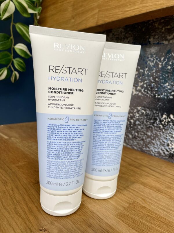 Two 200ml tubes of Re/Start Hydration Moisture Melting Conditioner are displayed on a wooden surface with a plant and blue wall behind, showcasing luxurious hydration and moisture care for your hair. Two 200ml tubes of Re/Start Hydration Moisture Melting Conditioner are displayed on a wooden surface with a plant and blue wall behind, showcasing luxurious hydration and moisture care for your hair.