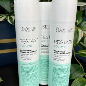 Three bottles of Re/Start Volume Magnifying Micellar Shampoo (250ml each) are displayed upright with green plants in the background, showcasing their volume-boosting formula.