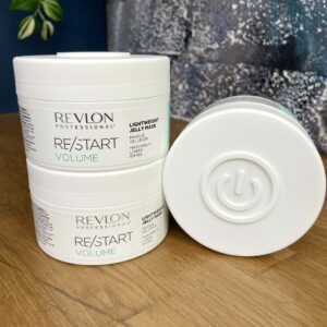 Three containers of Re/Start Volume Lightweight Jelly Mask are stacked on a wooden surface, showcasing its nourishing formula and the distinct power symbol featured on each container’s base.