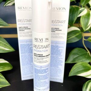 Three bottles of Re/Start Hydration Anti-Frizz Moisturising Drops are displayed before lush green plants, emphasizing their hydrating and anti-frizz benefits for smooth, healthy hair.