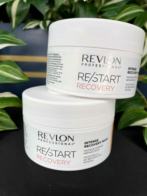 Two stacked tubs of Re/Start Recovery Intense Recovery Mask are displayed on a black surface, with lush green plants in the background. Two stacked tubs of Re/Start Recovery Intense Recovery Mask are displayed on a black surface, with lush green plants in the background.