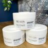 Three containers of Re/Start Curls Deep Nourishing Buttery Mask are stacked on a wooden surface, with a plant and blue wall in the background.