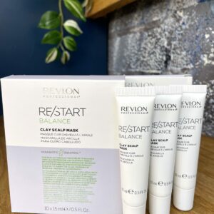 Three tubes and a box of Re/Start Balance Clay Scalp Mask sit on a wooden surface with green leaves in the background, highlighting this mask designed to help balance scalp health.