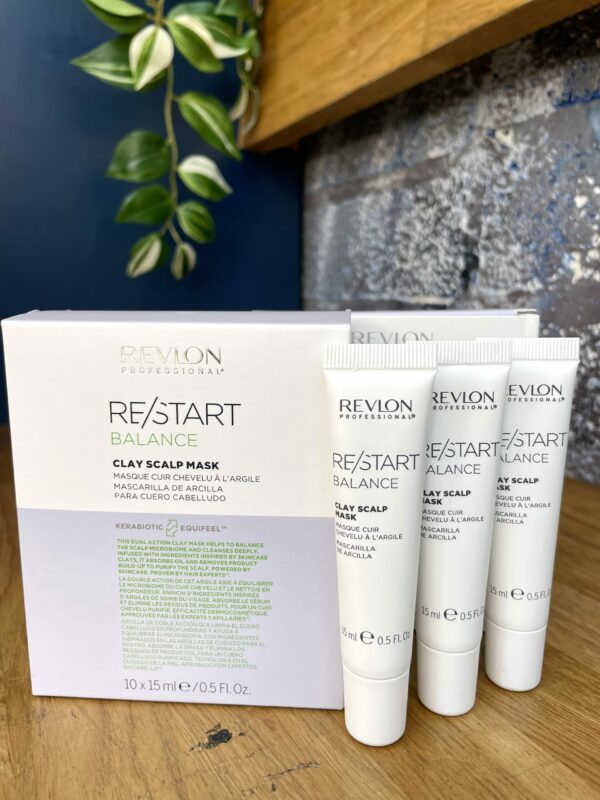 Three tubes and a box of Re/Start Balance Clay Scalp Mask sit on a wooden surface with green leaves in the background, highlighting this mask designed to help balance scalp health. Three tubes and a box of Re/Start Balance Clay Scalp Mask sit on a wooden surface with green leaves in the background, highlighting this mask designed to help balance scalp health.