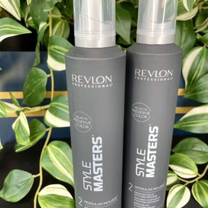 Two upright Style Masters Modular Mousse 300ml bottles are shown on a black surface, with green leafy plants in the background.