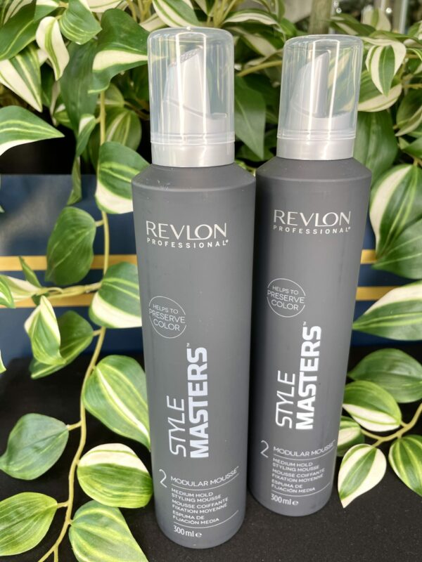 Two upright Style Masters Modular Mousse 300ml bottles are shown on a black surface, with green leafy plants in the background. Two upright Style Masters Modular Mousse 300ml bottles are shown on a black surface, with green leafy plants in the background.
