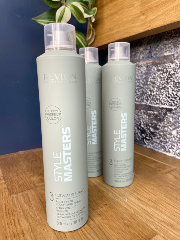 Three bottles of Style Masters Elevator Spray 300ml are displayed on a wooden shelf, with a plant and a blue textured wall in the background. Three bottles of Style Masters Elevator Spray 300ml are displayed on a wooden shelf, with a plant and a blue textured wall in the background.