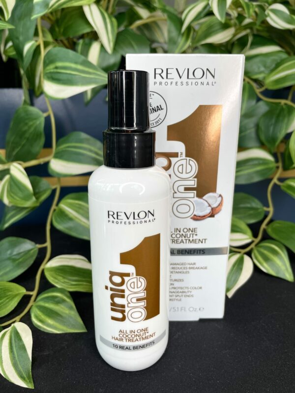 A bottle of UniqOne All in One Hair Treatment Coconut 150ml stands before its packaging, set against green leaves in the background.