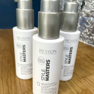 Three bottles of Style Masters Brightastic Shine Serum 100ml each are arranged on a wooden surface with a silver background.