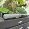 A Lizze Extreme Hair Straightener is placed on two stacked black boxes labeled Lizze Extreme Hair Straighteners, with green plants in the background.