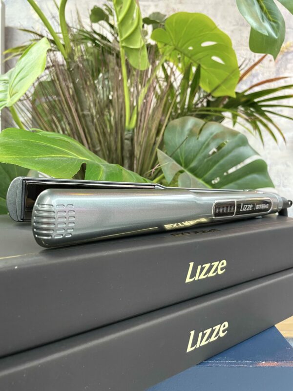 A Lizze Extreme Hair Straightener is placed on two stacked black boxes labeled Lizze Extreme Hair Straighteners, with green plants in the background. A Lizze Extreme Hair Straightener is placed on two stacked black boxes labeled Lizze Extreme Hair Straighteners, with green plants in the background.