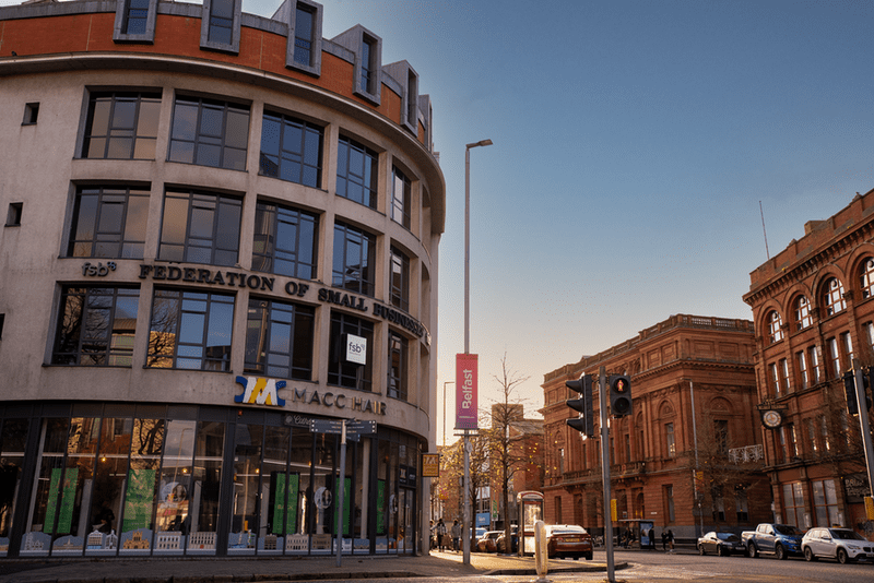 A curved modern building with "Federation of Small Businesses" signage on a city street corner, adjacent to red-brick historic buildings under a clear sky.